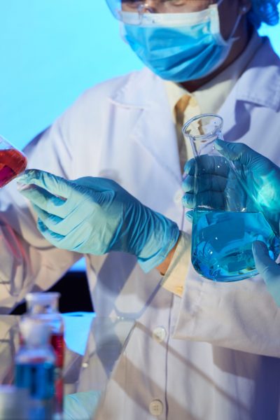 Group of chemists wearing safety goggles and white coats studying content of flasks while analyzing results of conducted experiment